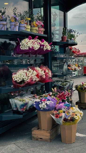 A display of fresh floral arrangements at floristcharingcross.co.uk, including bouquets of white and purple chrysanthemums wrapped in pink and purple tissue paper, alongside smaller vases of mixed flo